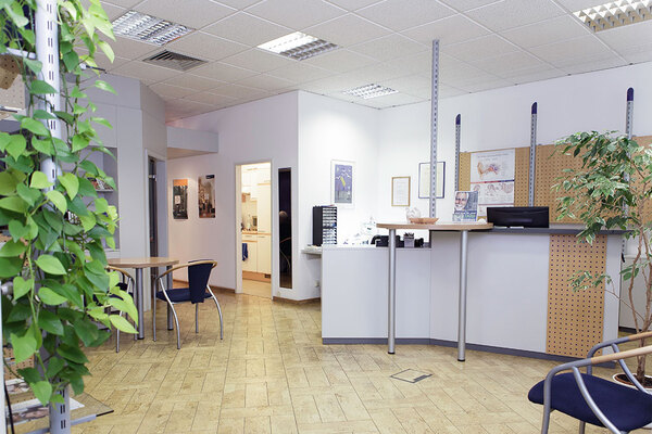 Heller Empfangsbereich mit Schreibtisch, Stühlen, Pflanzen und moderner Büroeinrichtung.